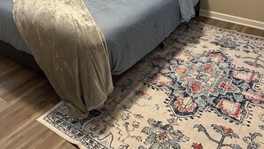 Ein Schlafzimmer mit einem Bett, einem gemusterten Teppich und zwei Wandbildern.