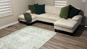 Ein Wohnzimmer mit einem Ecksofa, einem grünen Sessel und einem gemusterten Teppich.