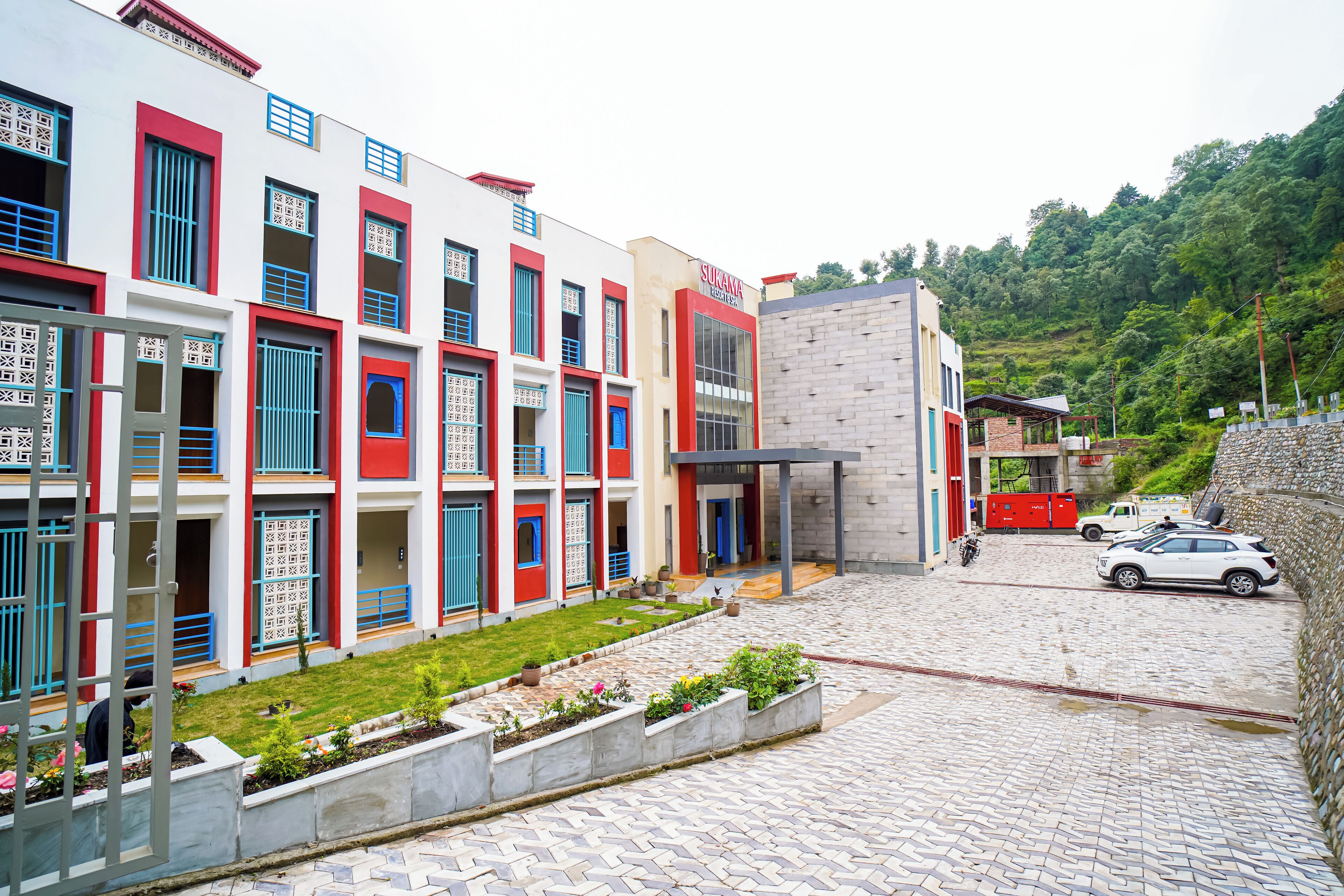 Edificio a più piani con cortile interno, ingresso coperto e area parcheggio con veicoli.