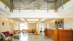 A spacious lobby with a wooden reception desk, comfortable seating areas, and a mezzanine level with a railing. - Sukama Resort & Spa (Dhari)