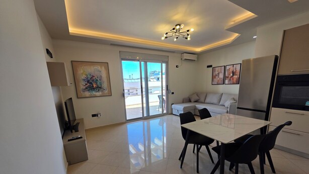 A modern living room with a dining area, a sofa, a TV, and a painting on the wall. - Thomas K Veranda Apartment (Vlorë)