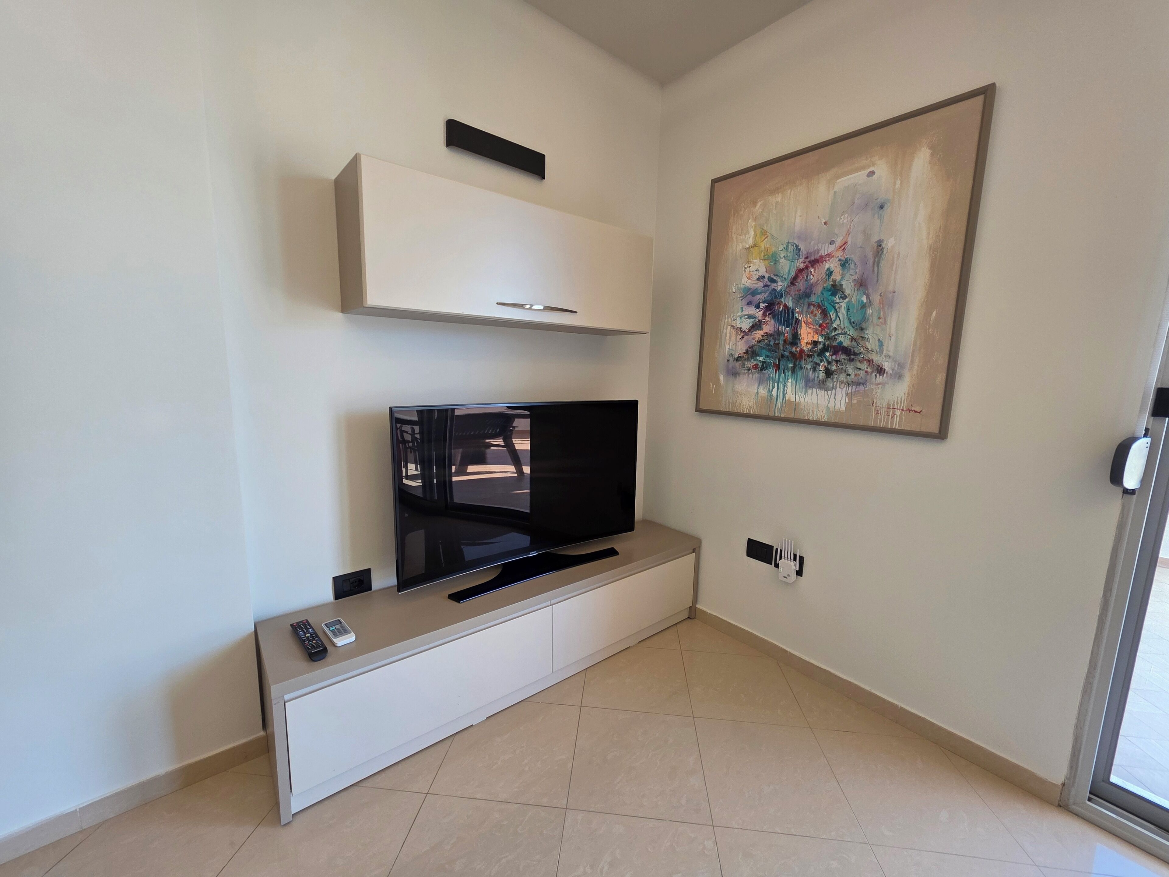 Ein modernes Wohnzimmer mit Flachbildfernseher, Schrank und einem Gemälde an der Wand.