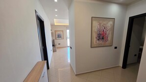 A hallway with a wooden bench, a painting on the wall, and a tiled floor. - Thomas K Veranda Apartment (Vlorë)