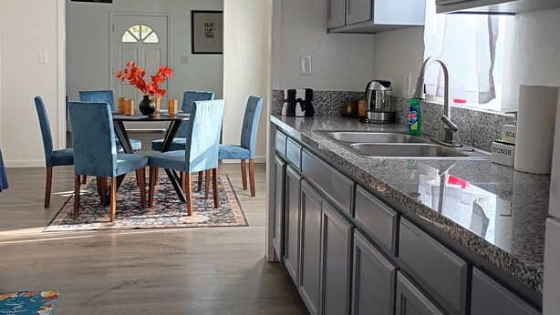 Een moderne keuken met grijze kastjes, een granieten aanrechtblad en een eethoek met blauwe stoelen en een vloerkleed met bloemenmotief.
