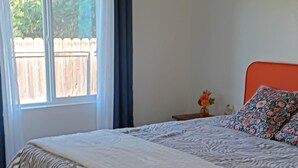 Een slaapkamer met een groot bed, een raam met gordijnen, een houten vloer en een plafondventilator.