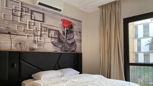 A bedroom with a bed, a headboard with a geometric design, a red rose decoration, and a window with a view of buildings. - 3-bedroom apartment in perfect  Giza Governorate, Beverly Hills, Sheikh Zayed. (Giza Governorate)