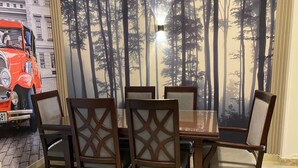A dining table with six wooden chairs, a red vintage car in the background, and a forest-themed wall mural. - 3-bedroom apartment in perfect  Giza Governorate, Beverly Hills, Sheikh Zayed. (Giza Governorate)