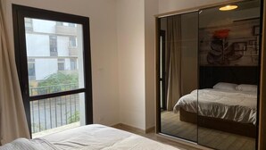A bedroom with a large sliding glass door leading to a balcony, a bed with white bedding, and a wooden floor. - 3-bedroom apartment in perfect  Giza Governorate, Beverly Hills, Sheikh Zayed. (Giza Governorate)