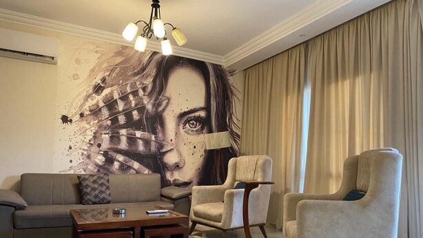 A living room with a sofa, armchairs, a coffee table, a lamp, and a wall mural. - 3-bedroom apartment in perfect  Giza Governorate, Beverly Hills, Sheikh Zayed. (Giza Governorate)