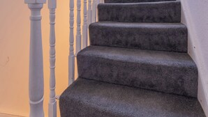 A staircase with white balusters and dark carpeted steps leading to a landing with a small window.