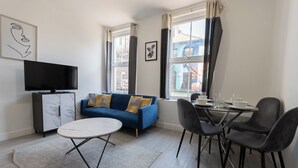 A modern living room with a blue sofa, a white coffee table, and a dining area with black chairs.