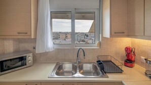 A kitchen with a double sink, a microwave, a red coffee maker, and a window with a view of buildings. - Sunlit Terrace 3BR Apartment – Tavros by ΜΡS (Tavros)