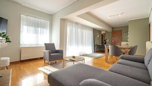 A modern living room with a grey sofa, a round coffee table, and a dining area with a wooden table and chairs. - Sunlit Terrace 3BR Apartment – Tavros by ΜΡS (Tavros)