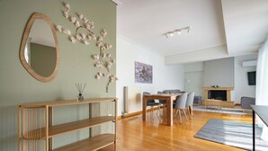 A modern living room with a wooden console table, a dining area with a table and chairs, a fireplace, and a large mirror on the wall. - Sunlit Terrace 3BR Apartment – Tavros by ΜΡS (Tavros)