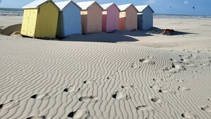 A row of beach huts with a sandy beach and footprints in the foreground.