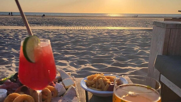 A beachside table with a drink, snacks, and a sunset view.