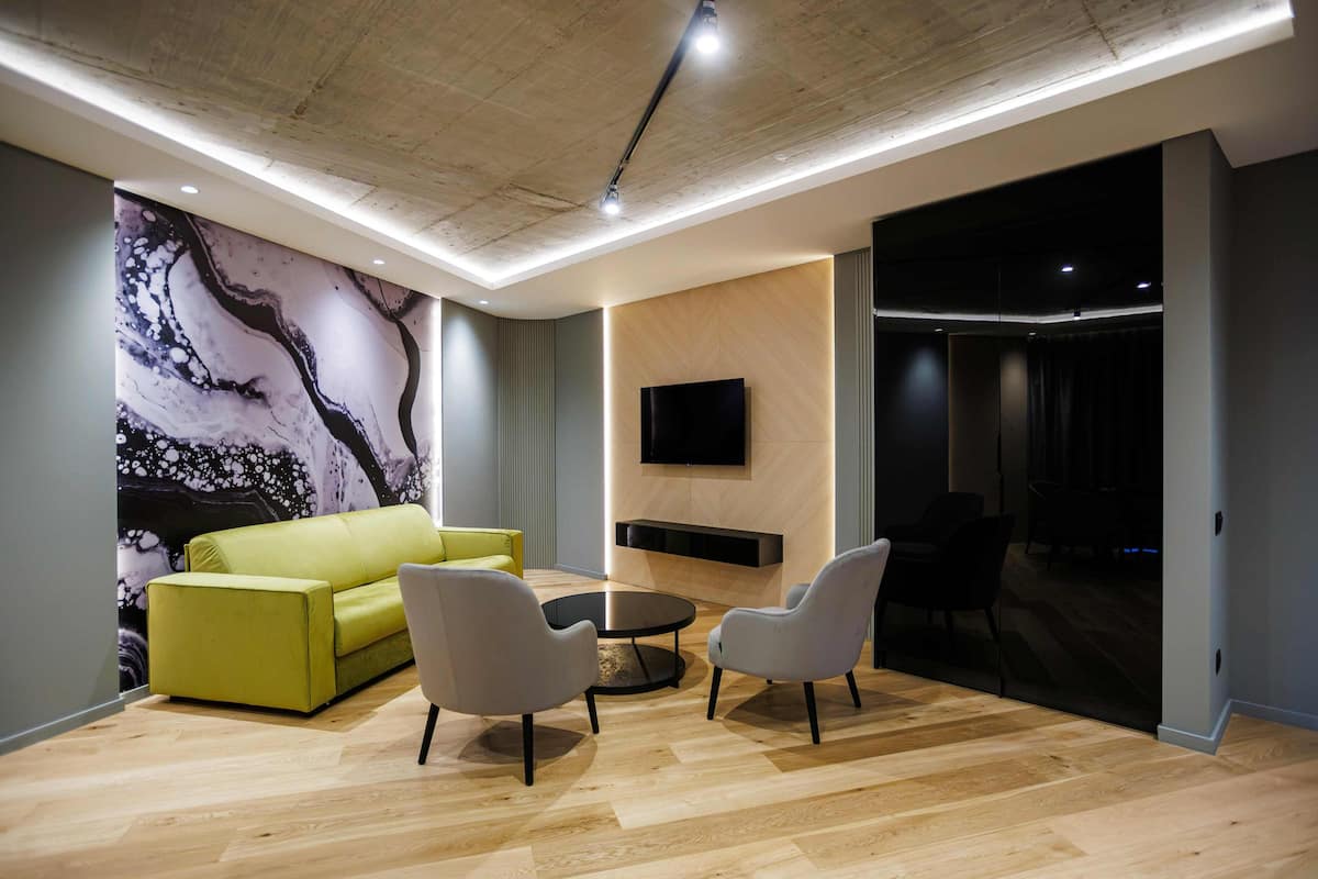 A modern living room with a green sofa, two armchairs, a coffee table, and a large abstract mural on the wall.