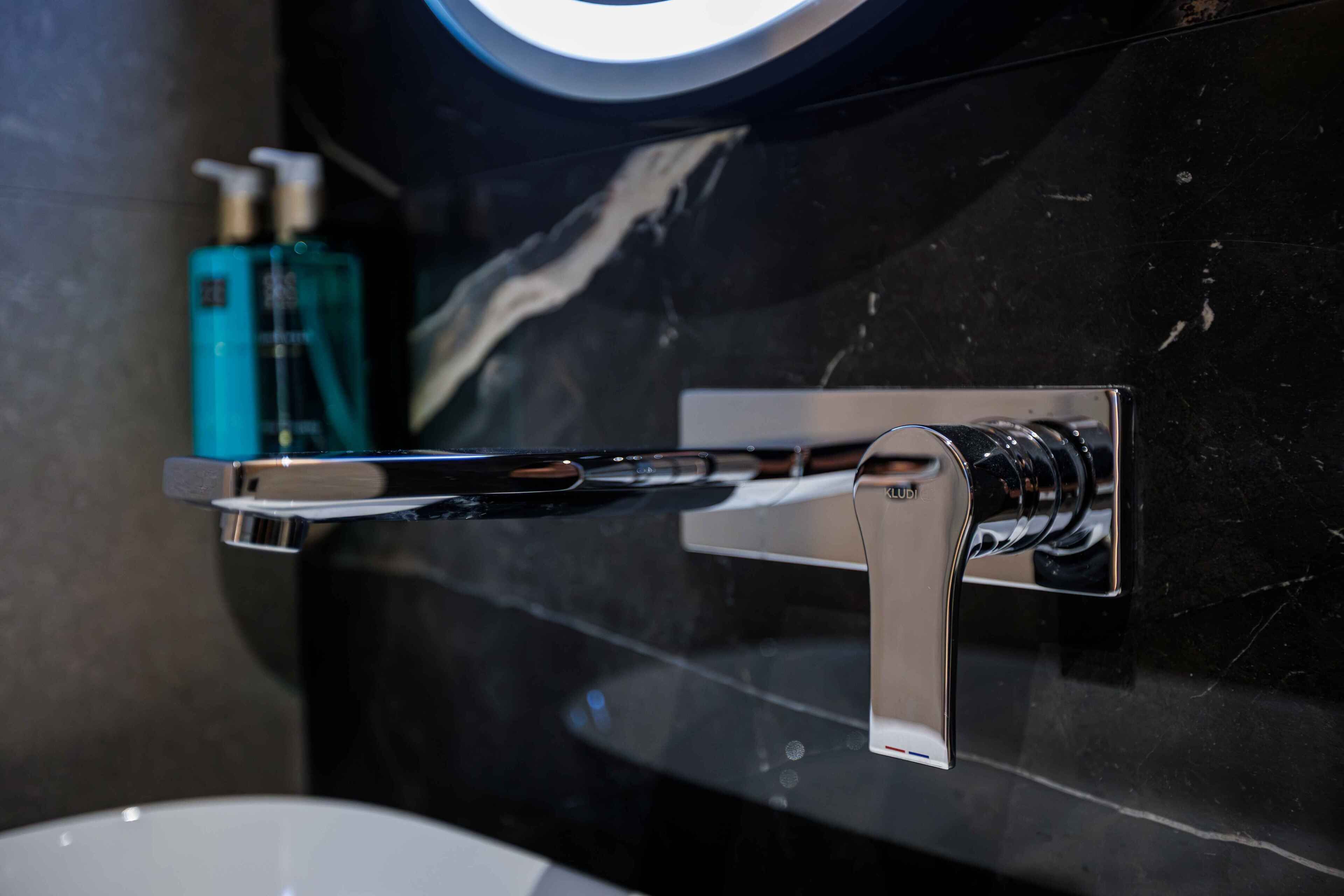 A chrome faucet mounted on a black marble wall with a white sink below.