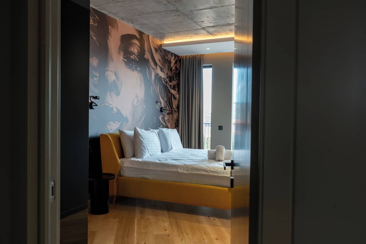 A modern bedroom with a bed, a wall mural, a window, and a door.