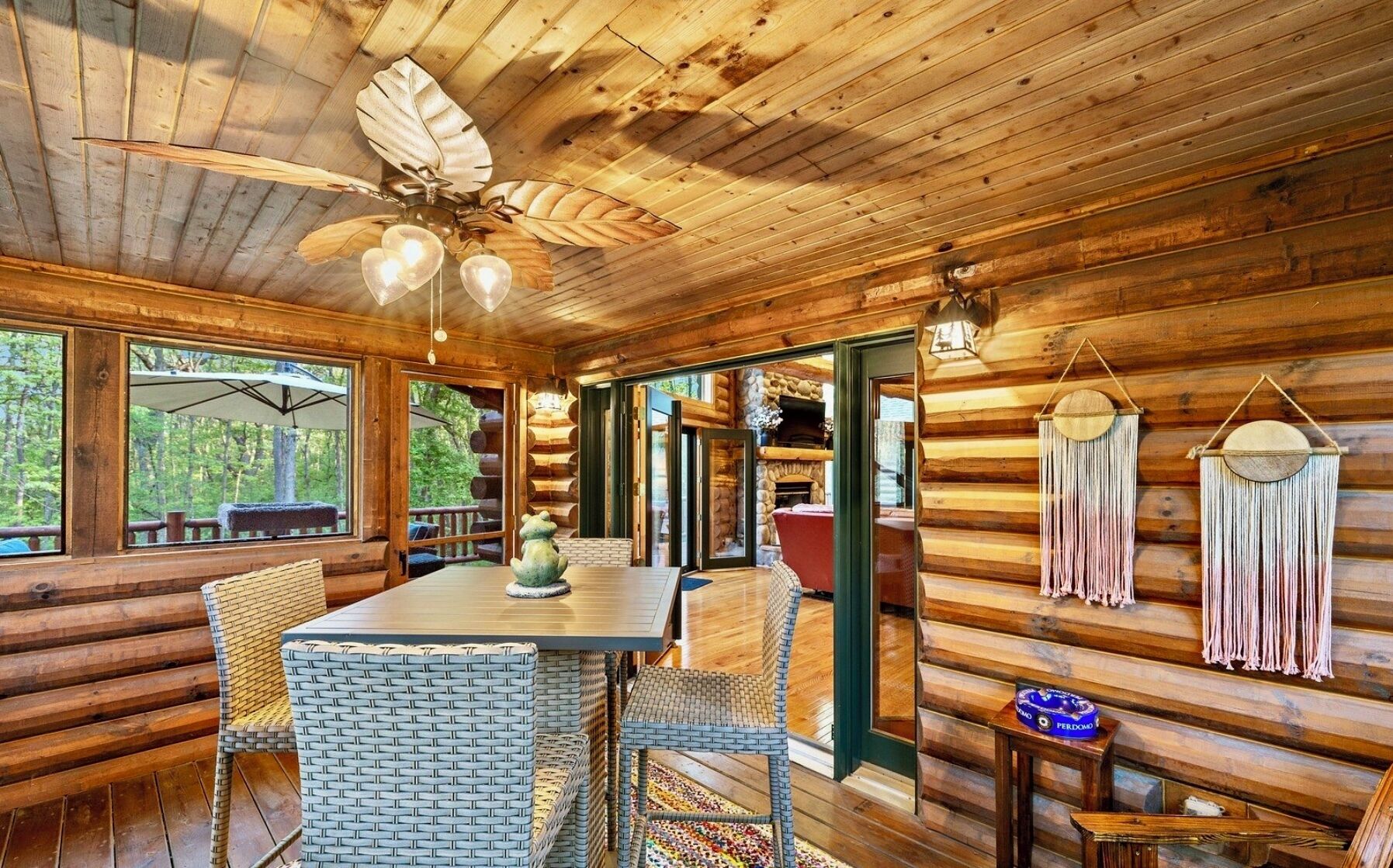 L’intérieur d’une cabane en rondins comprend un coin repas, des chaises en osier, une cheminée et un ventilateur de plafond.