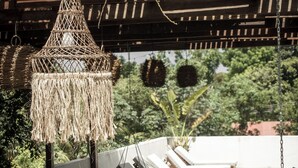 Un espace extérieur abrité, doté de fauteuils confortables, d’un luminaire suspendu et offrant une vue sur la verdure en arrière-plan.