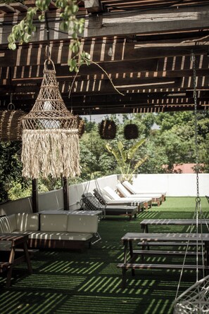 A covered outdoor seating area with lounge chairs, a hanging light fixture, and a view of greenery in the background. - Hotel Lydna Ki'n  (Bacalar)