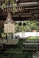 Un área de estar al aire libre con techo, sillones reclinables, una lámpara colgante y vistas a la vegetación de fondo.