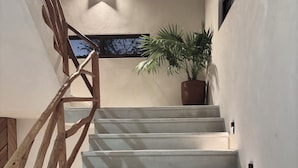 Un escalier en béton avec des rampes en bois, un pot de fleurs et un luminaire fixé au mur.