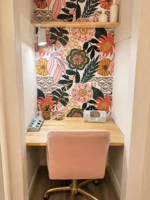 A corner desk with a floral wallpaper, a pink chair, and a shelf with decorative items. - Studio with Fireplace + bonus lounge & work area- fenced yard. (Lawrence)