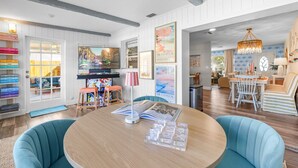 Una habitación con una mesa de madera, sillas color turquesa y una estantería llena de libros.