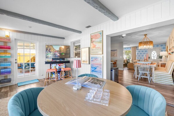 A room with a wooden table, teal chairs, and a bookshelf filled with books. - Sunshine Daydream: Heated Pool, Putt Putt, Arcade Room (Seminole)