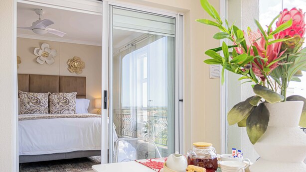 Ein Hotelzimmer mit Bett, Esstisch mit Frühstücksangeboten, Blumen in einer Vase und einem Balkon mit Blick.