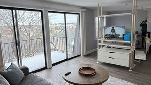 Een moderne woonkamer met een grijze bank, een ronde salontafel en een televisie op een witte dressoir.