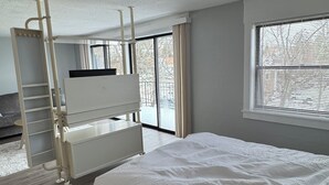 Een slaapkamer met een stapelbed, een bureau en een raam met jaloezieën.