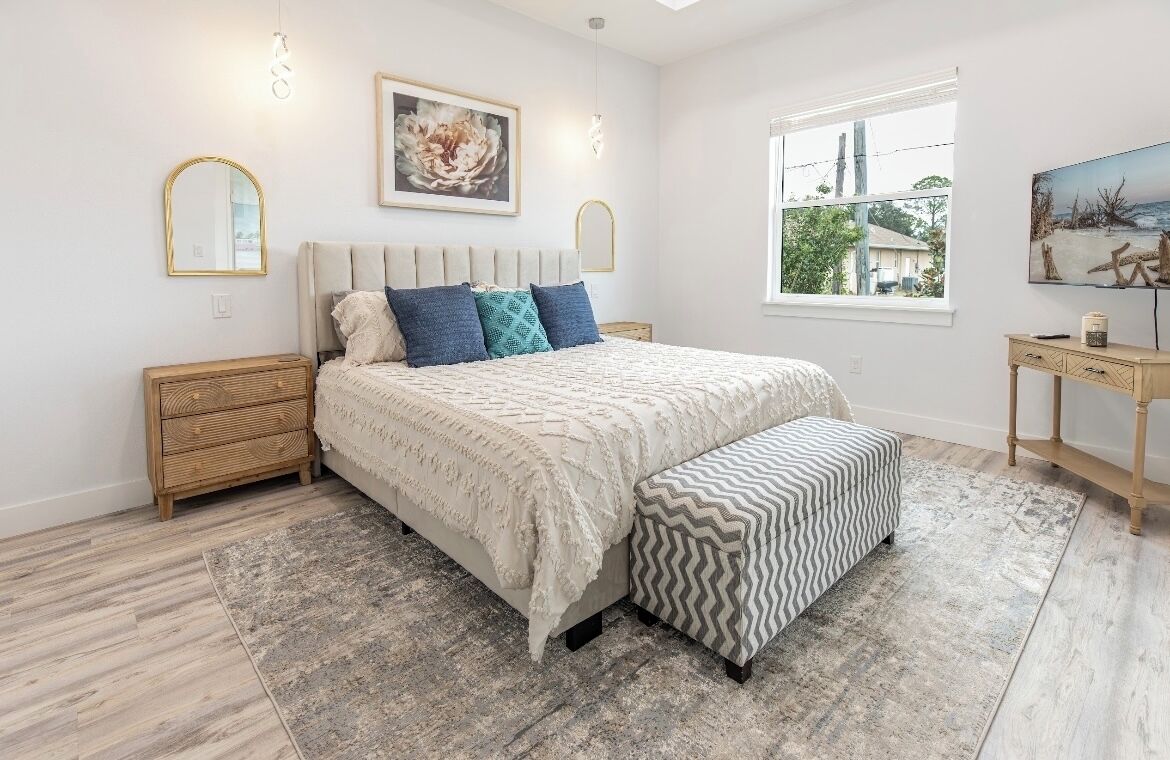 Een slaapkamer met een bed, nachtkastjes, een bankje, een vloerkleed en kunstwerken aan de muur.