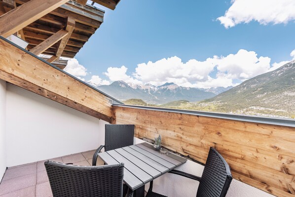 Un balcon en bois, agrémenté d’une table et de chaises, qui offre une vue sur un paysage montagneux.