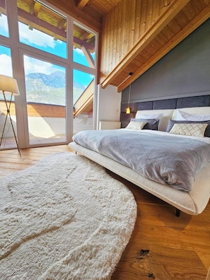 A bedroom with a bed, a large window, and a view of mountains.