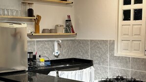 A modern kitchen with a black countertop, a built-in stove, and a microwave. There are wooden stools and a sink with a faucet. - Seu cantinho na Gamboa (Cabo Frio)