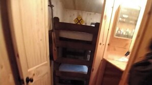 Un pasillo estrecho con suelo de madera, una cama litera y una puerta a la izquierda.