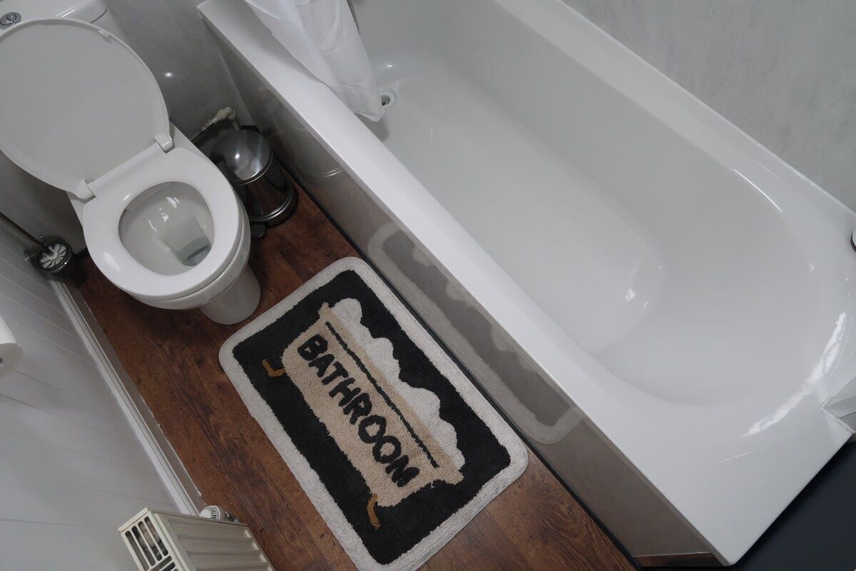A bathroom with a toilet, a bathtub, and a doormat with the word 'BATHROOM' on it.
