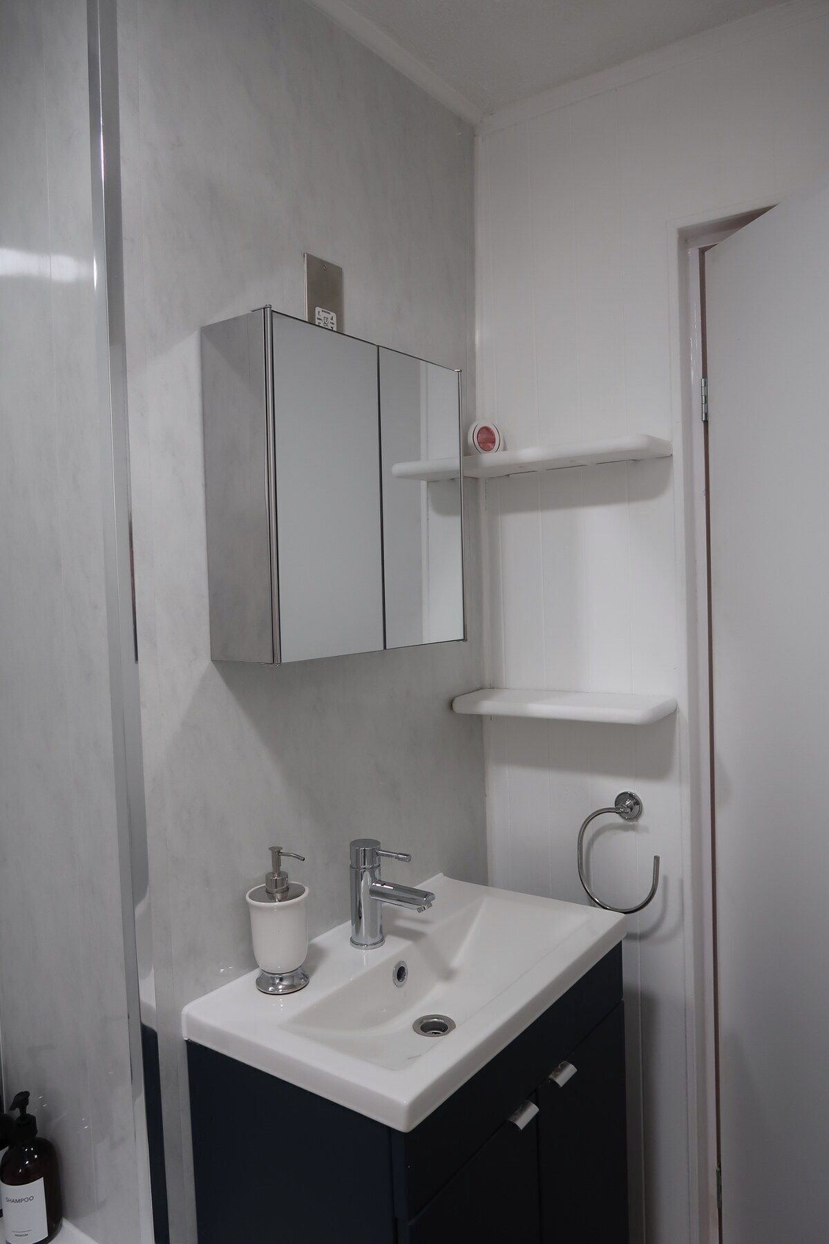 Ein Badezimmer mit einem weißen Waschbecken, einem Spiegel, einem Schrank und einem Toilettenpapierhalter.