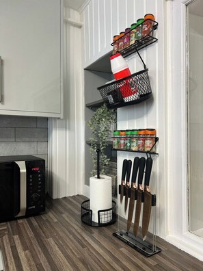 Una cocina con microondas, dispensador de toallas de papel, frascos de especias y bloque de cuchillos.
