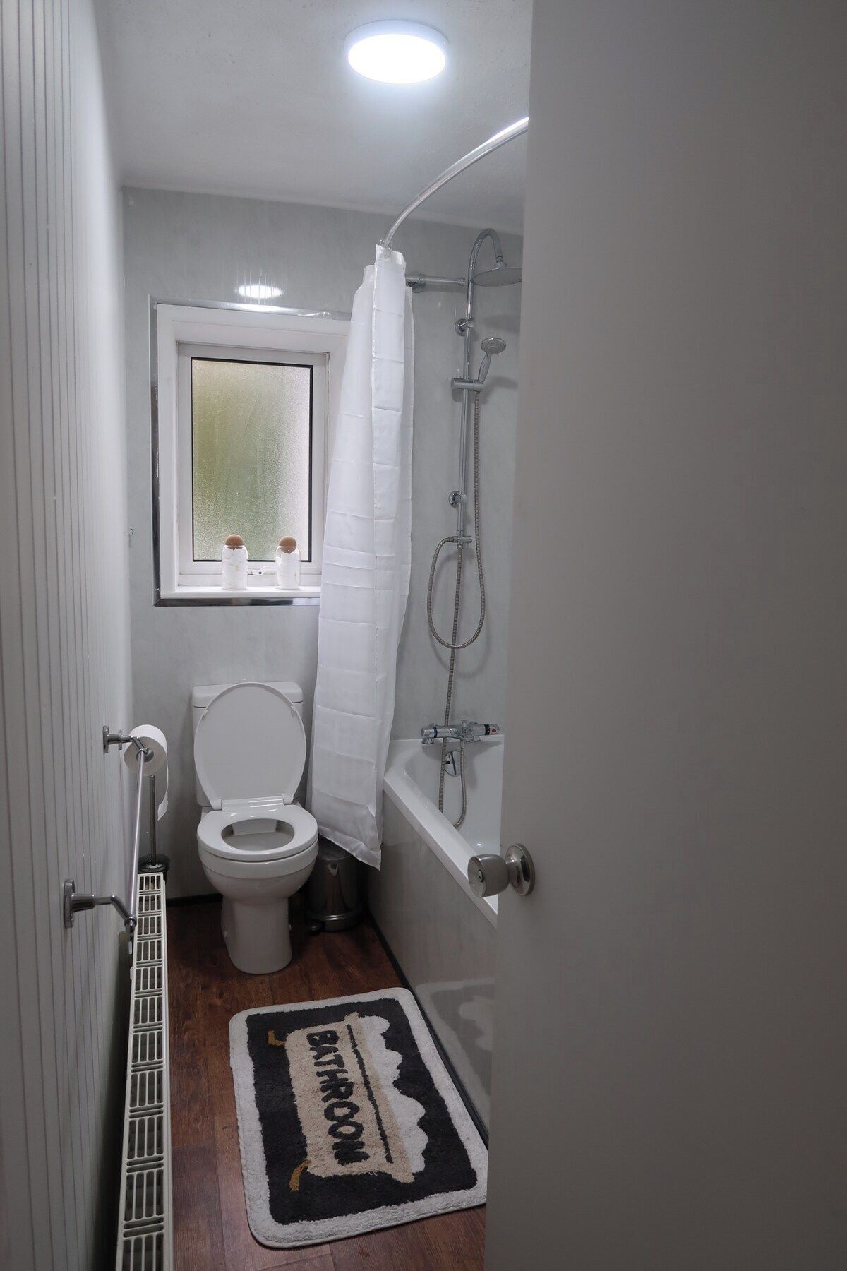 A compact bathroom with a toilet, shower, and a window above the toilet.