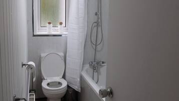 A compact bathroom with a toilet, shower, and a window above the toilet.