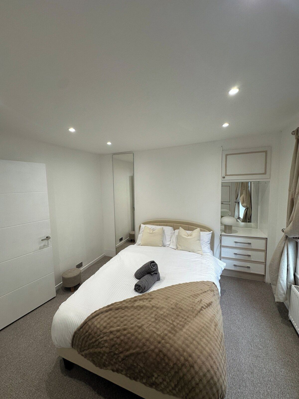 A hotel room with a large bed, a bedside table, a mirror, a wardrobe, and a bathroom with a shower and a toilet.