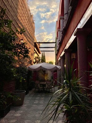 A narrow alleyway with a table and chairs under a canopy, surrounded by potted plants and a brick wall. - Encantadora Casa en el corazón de SMA (San Miguel de Allende)