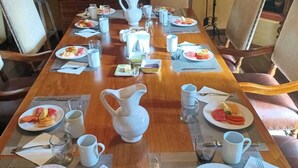 Une table à manger dressée pour le petit-déjeuner, avec des assiettes de fruits, des tasses et un pichet.