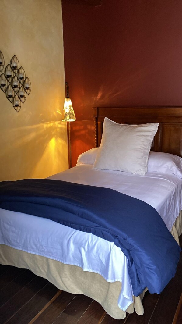 Un lit bien fait, avec une literie blanche et bleue, une tête de lit en bois et un luminaire fixé au mur.