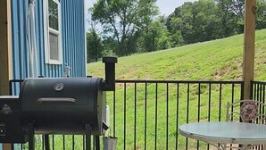 Ein überdachter Außenbereich mit Grill, Tisch und einem blauen Gebäude im Hintergrund.