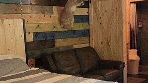 Ein Schlafzimmer mit einem Bett, einem hölzernen Kopfteil mit einem Hirschmotiv, einem Ledersofa und einer Holztür.